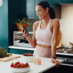 Self-care Simplified: Over-the-Counter Remedies You Can Get at Independent Pharmacy. House, fitness and woman in kitchen, smartphone and smile with fruit, typing and online reading for diet. Person, apartment or athlete with sportswear, cellphone or nutrition with social media or app